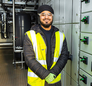 Young smiling man stands next to control panel in industrial building.
