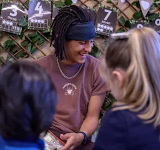 A young man sits next to some children in a nursery.