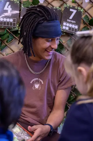 A young man sits next to some children in a nursery.