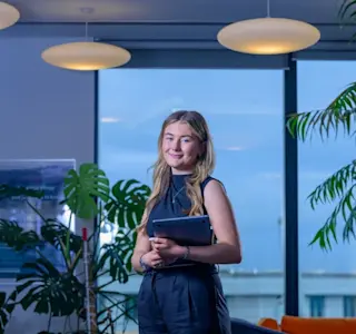 A young woman holds a laptop in her arms in an office environment.