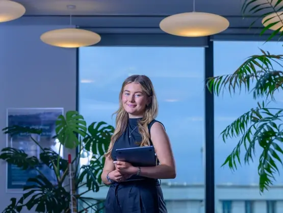 A young woman holds a laptop in her arms in an office environment.