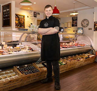 Young smiling man in black uniform, standing next to food counter in a shop