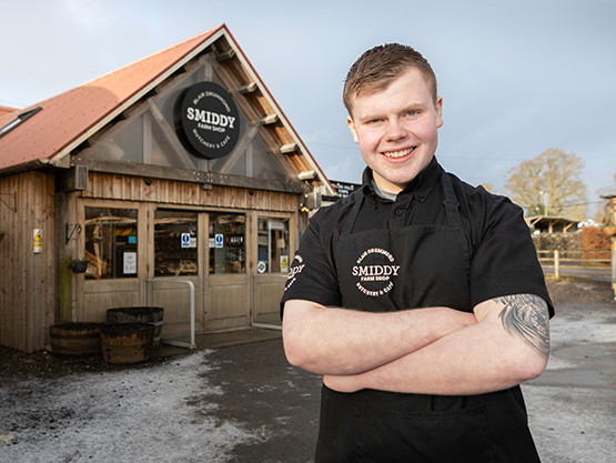 Young smiling man in black work clothing. standing in front of farm shop