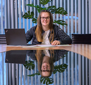 A woman sits behind a desk and uses a laptop computer.