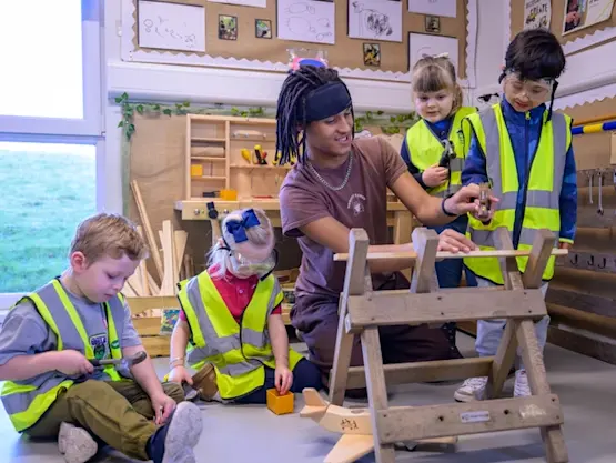 A young man helps children work on a woodwork project.