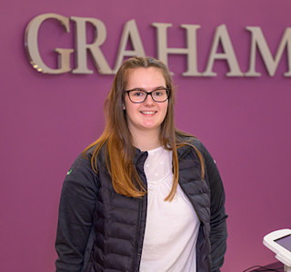 A woman stands in front of a purple wall with a GRAHAM sign on it.
