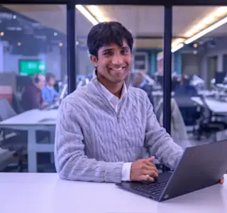 A young man uses a laptop at his desk within an office meeting room.