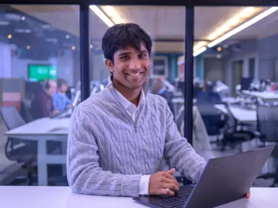A young man uses a laptop at his desk within an office meeting room.