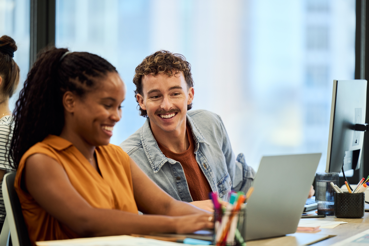 Two coworkers looking and laughing at a laptop.