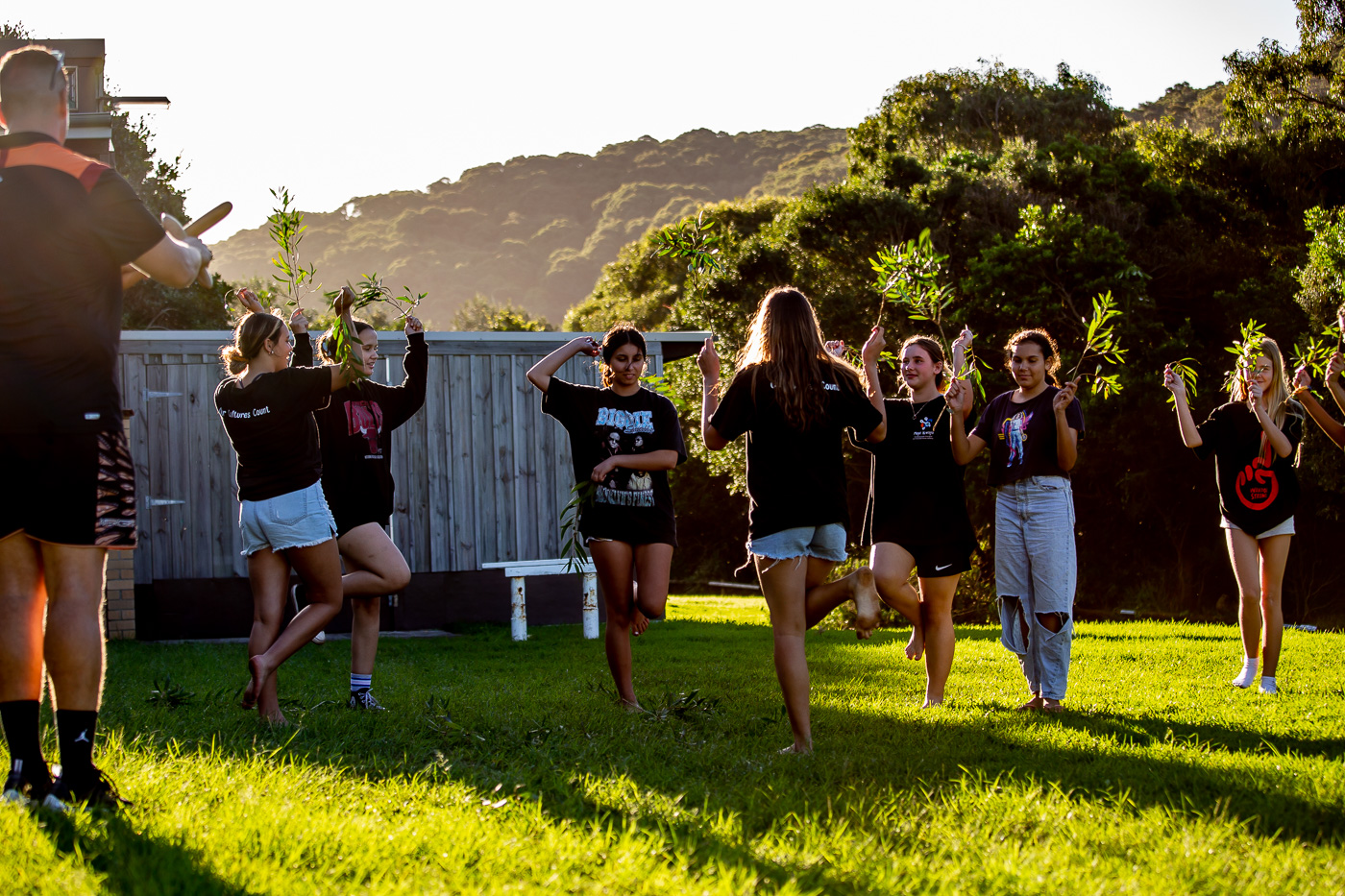 A group of teenage girls outside on the grass learning a First Nations traditional dance