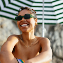 Woman smiling and wearing sunglasses at the beach.