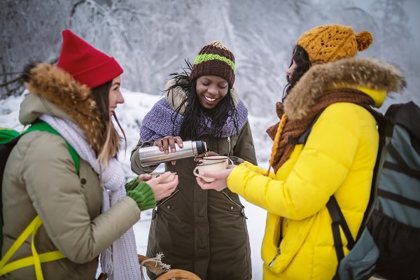 Three women in the snow, warming up by drinking a warm drink from a thermos