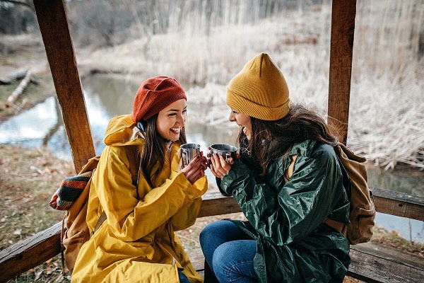 Two women sitting in a snowy climate, drinking a warm cup of liquid