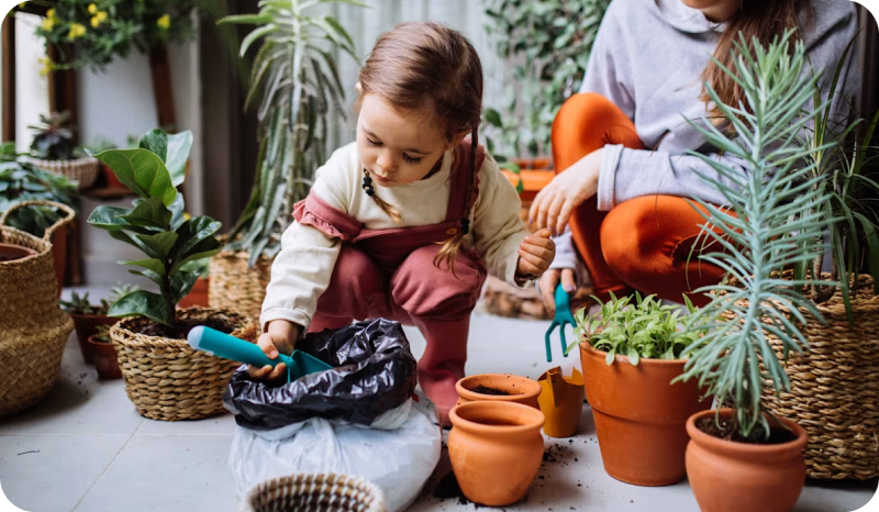 Young child wearing overalls and her mum surrounded by plants and doing some gardening