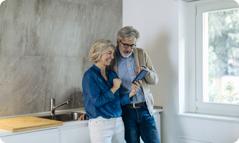 Mature couple using cell phone together in kitchen at home