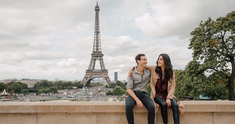 A smiling couple sitting in front of the Eiffel Tower, Paris, France.