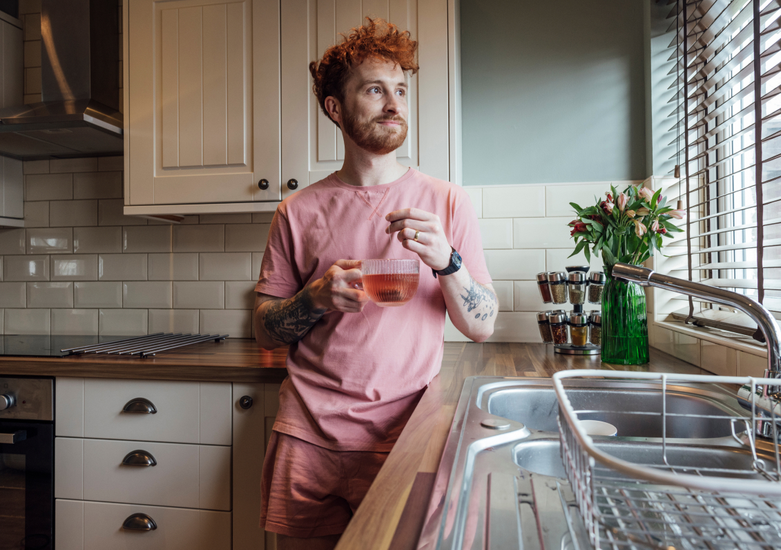 A man holding a cup of tea in his kitchen.