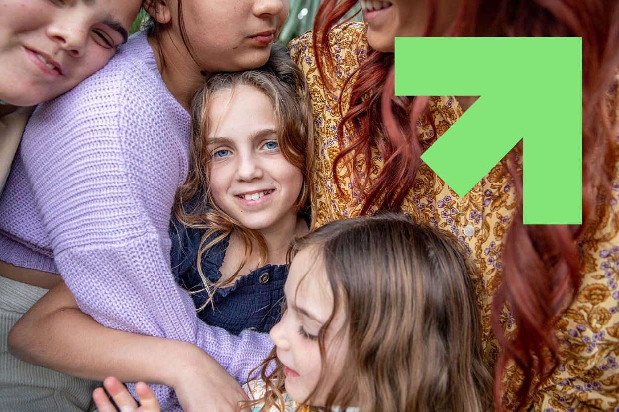 Group of kids hugging each other, with green arrow in the top right pointing up