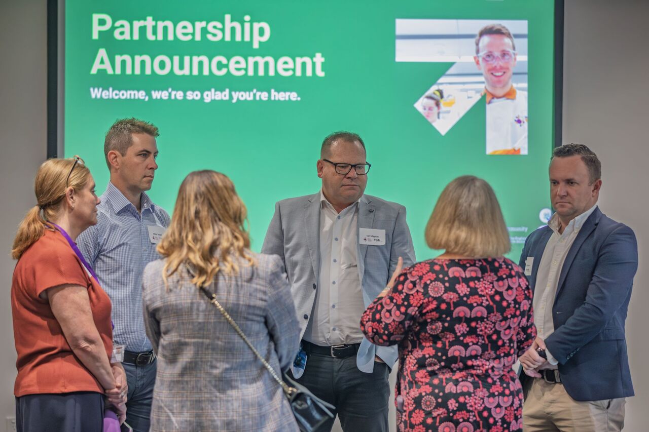 Attendees from nib and HMRI talk in front of a large screen with the partnership announcement