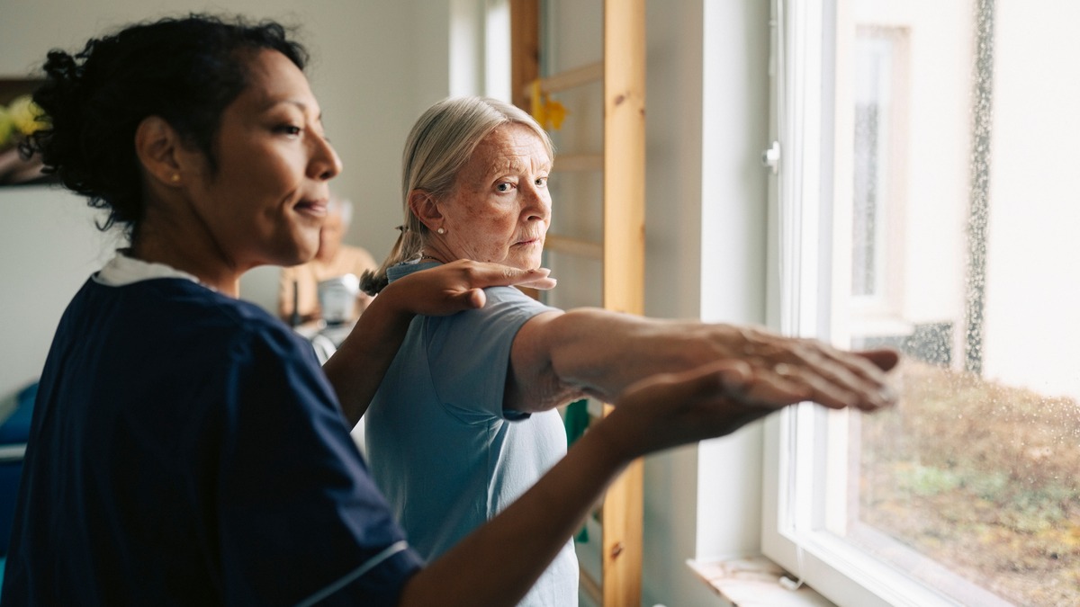 A woman doing stretches with the assistance of a nurse.