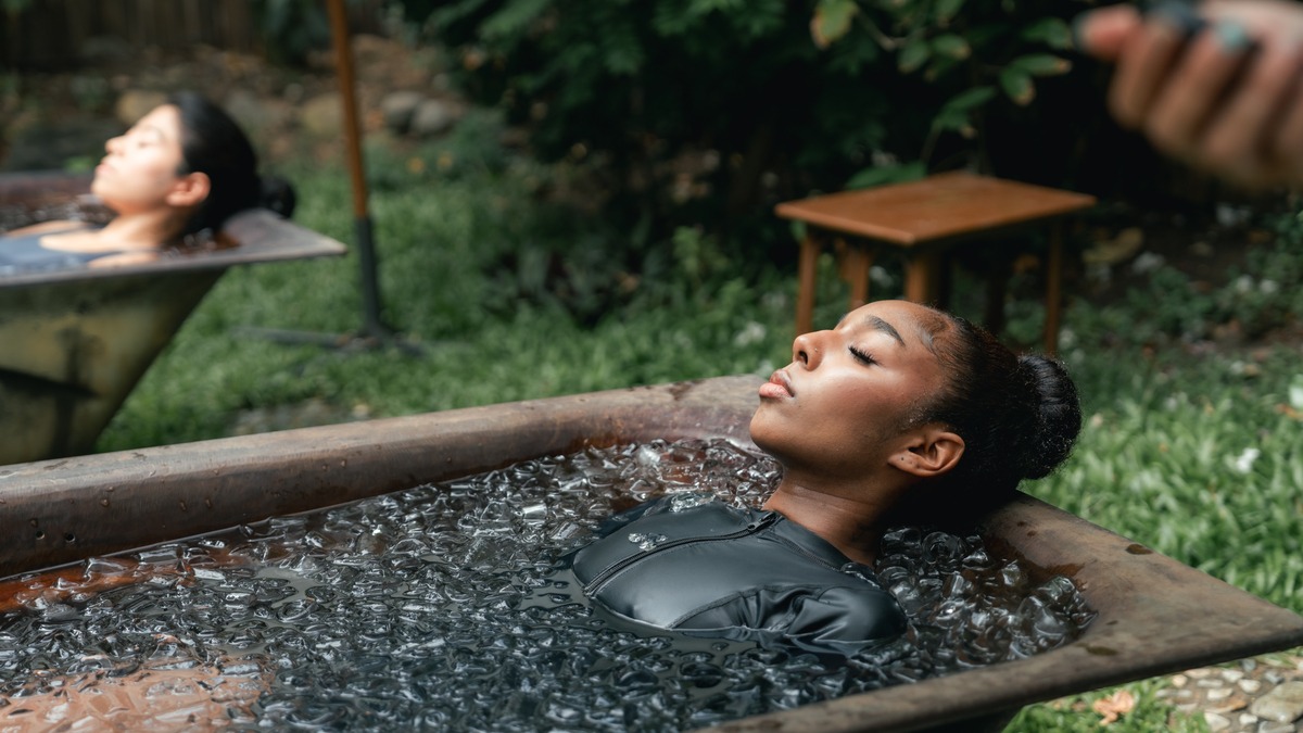 Person in an ice bath, with a friend in a separate ice bath in the background.