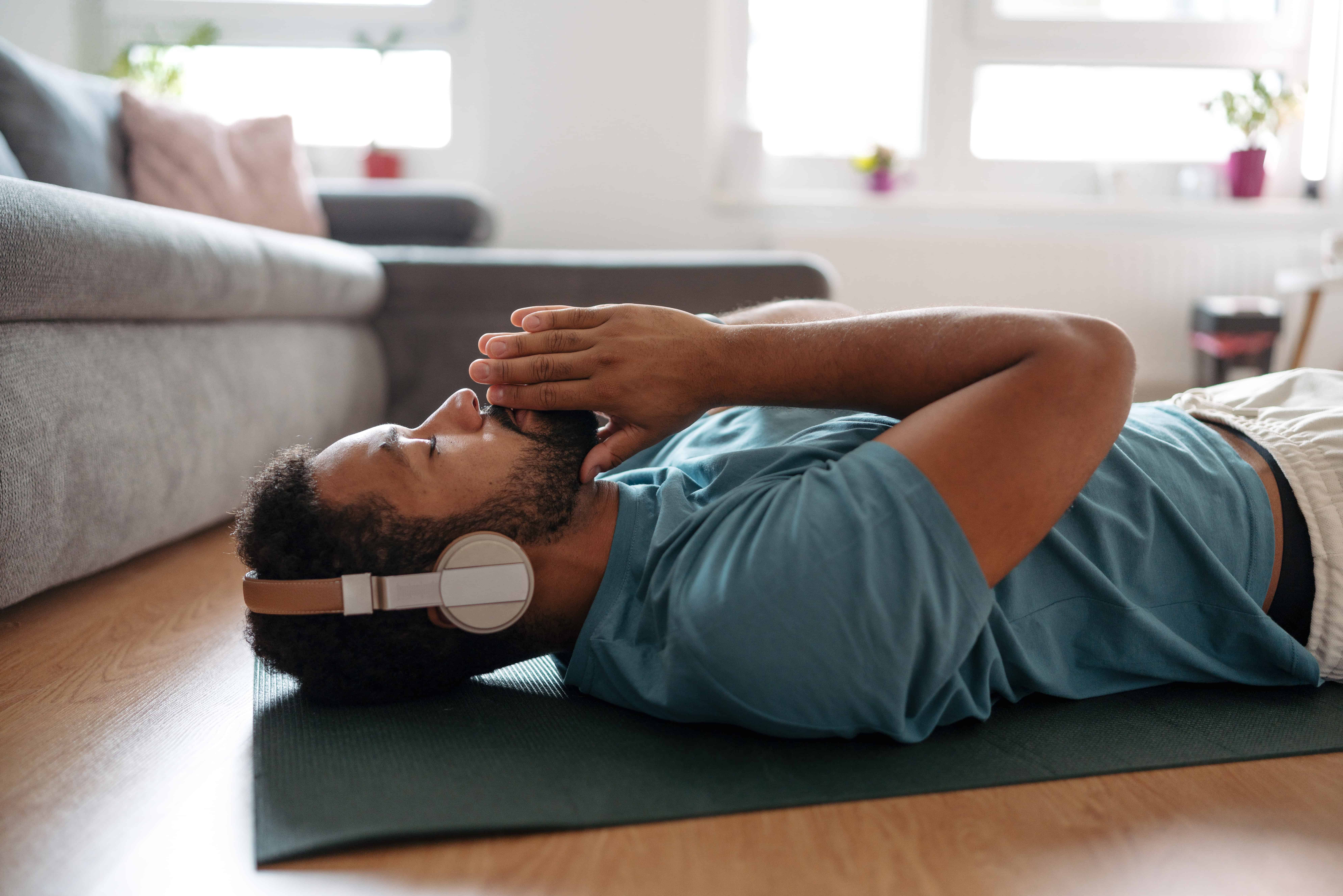 Person laying on their back on the floor, hands to their face.