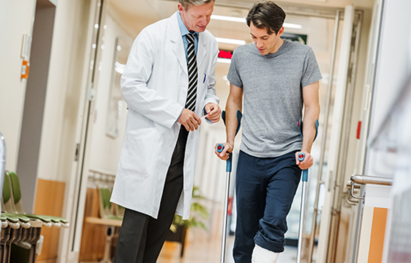 Doctor helping young man walk with crutches at the hospital