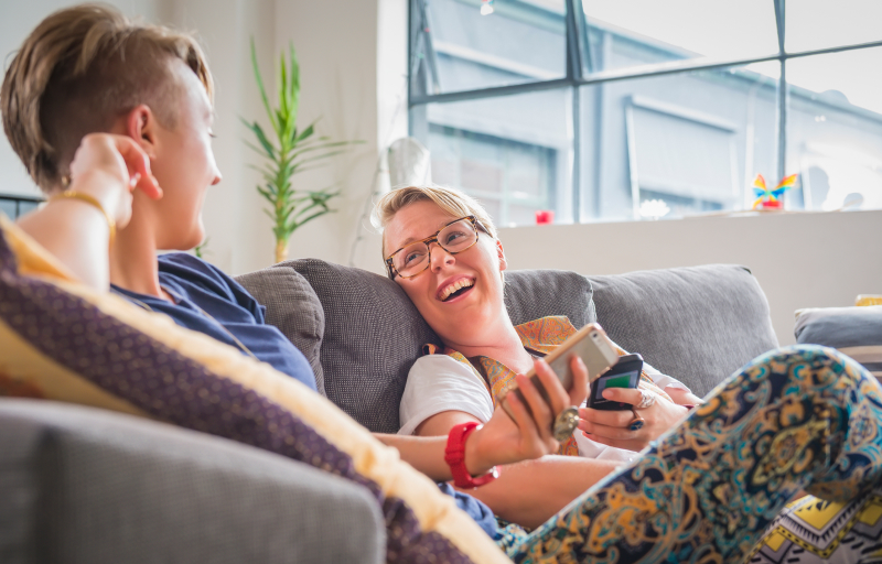 Queer women couple on the couch holding phones and smiling