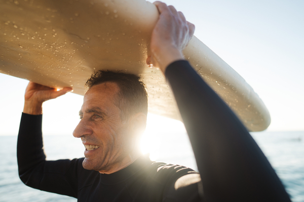 A man carrying his surfboard over his head at sunrise.