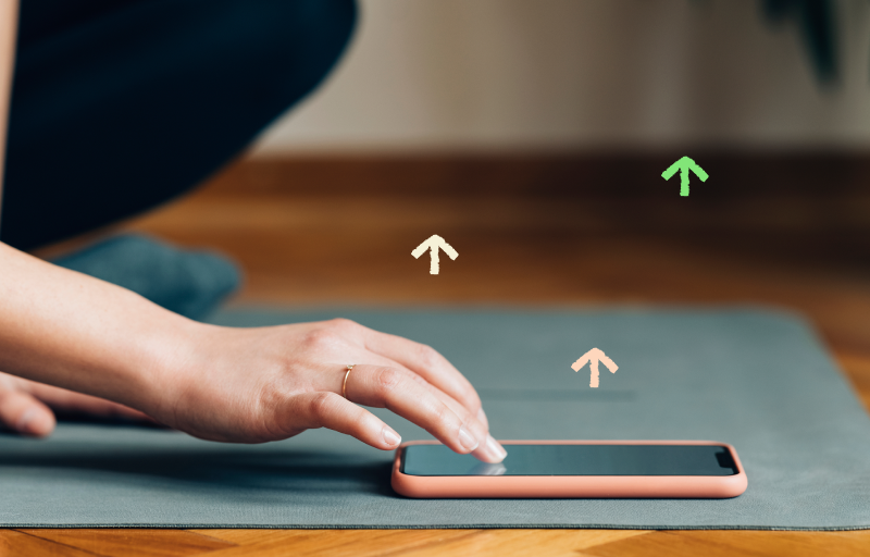 Woman checking her phone on a yoga mat with illustrations of arrows pointing upwards.