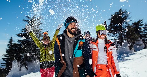 Three people in the snow smiling, wearing snow clothes. One women is throwing snow in the end so it showers the others