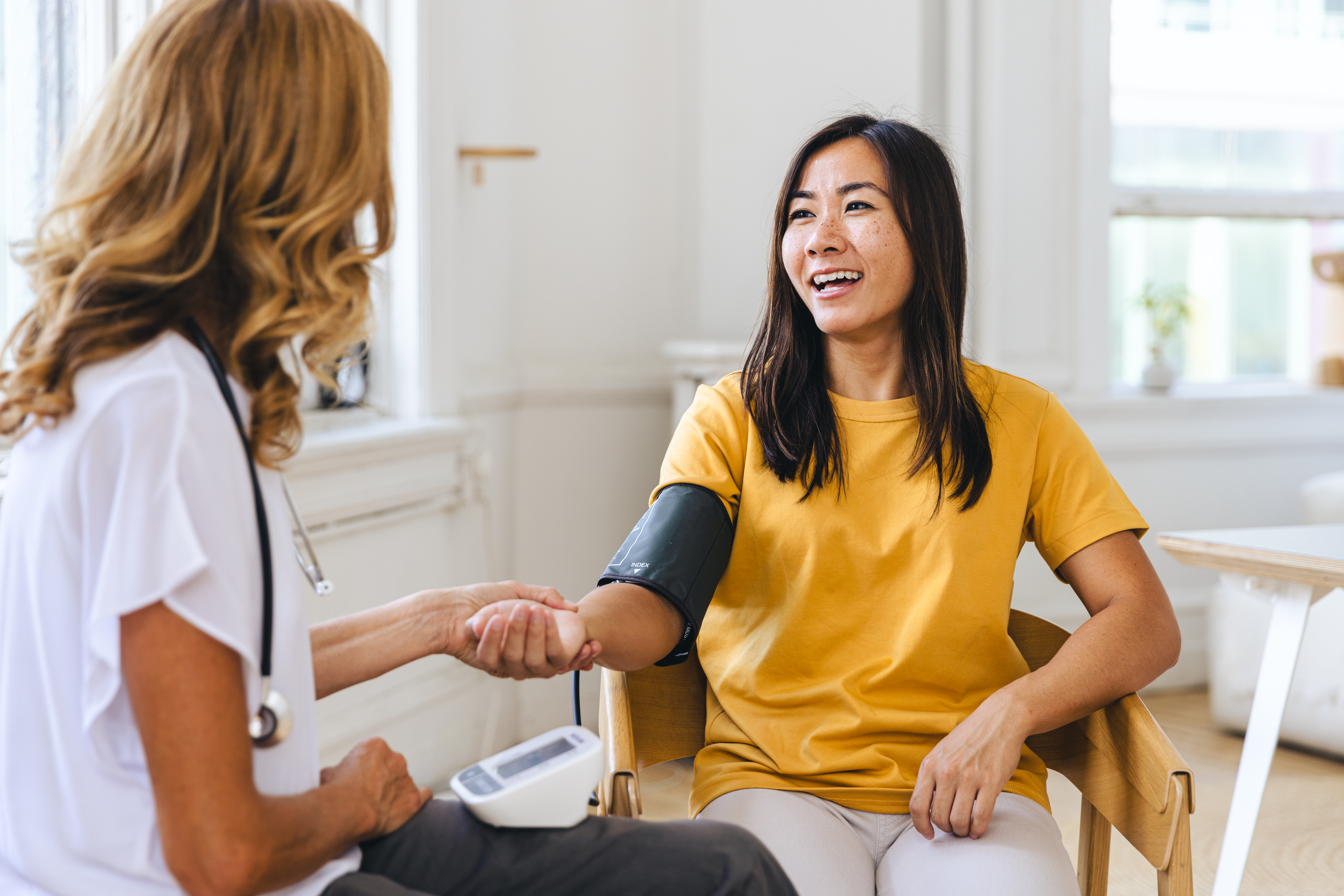 Woman sitting in chair having her blood pressure checked by a female doctor