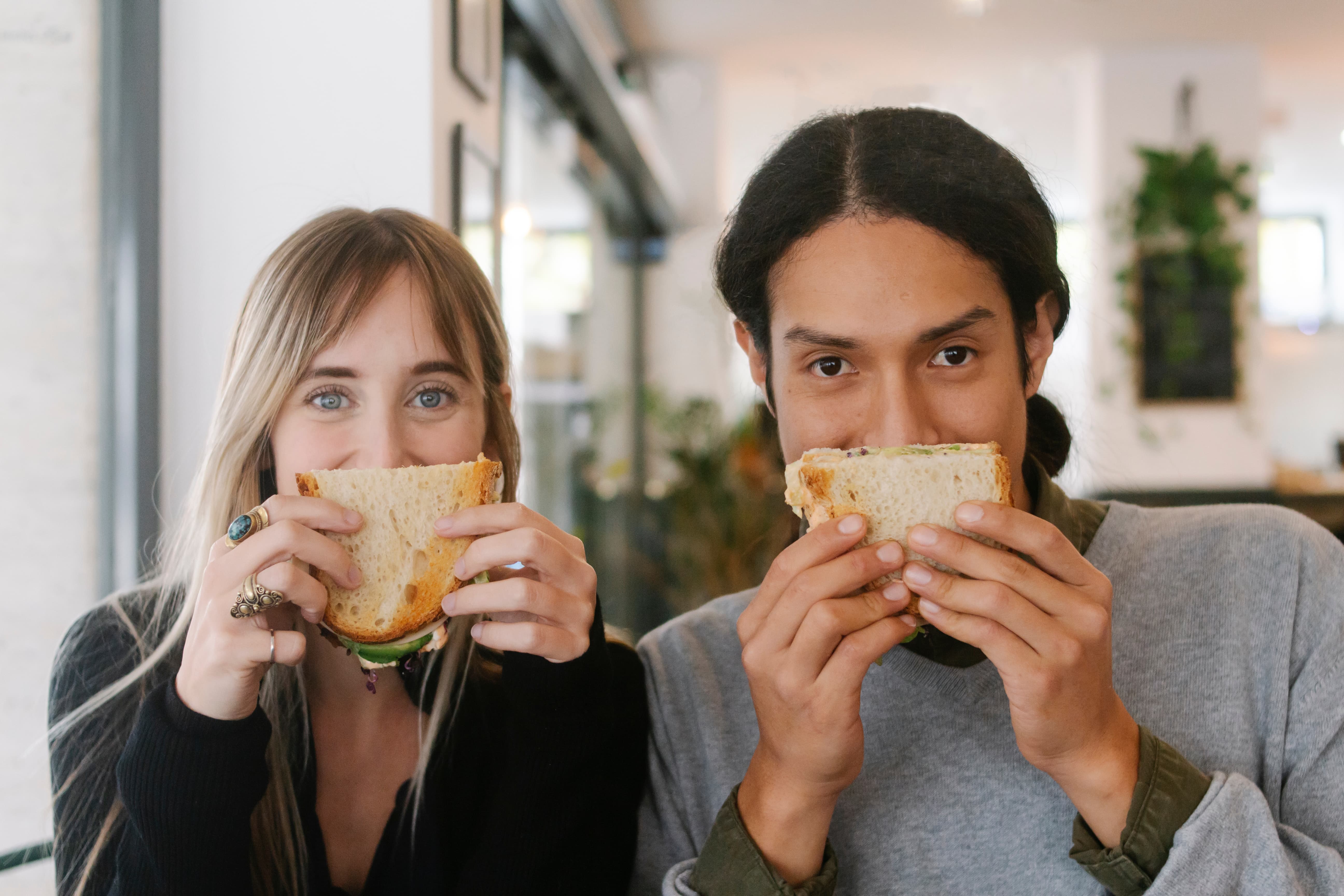 Two people peaking over the top of sandwiches.