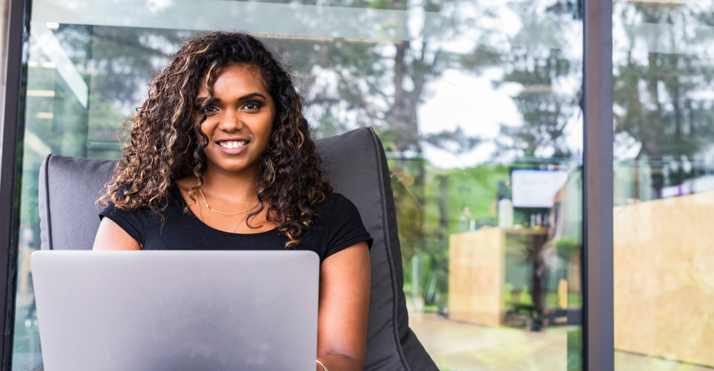 A woman sitting and smiling with a laptop