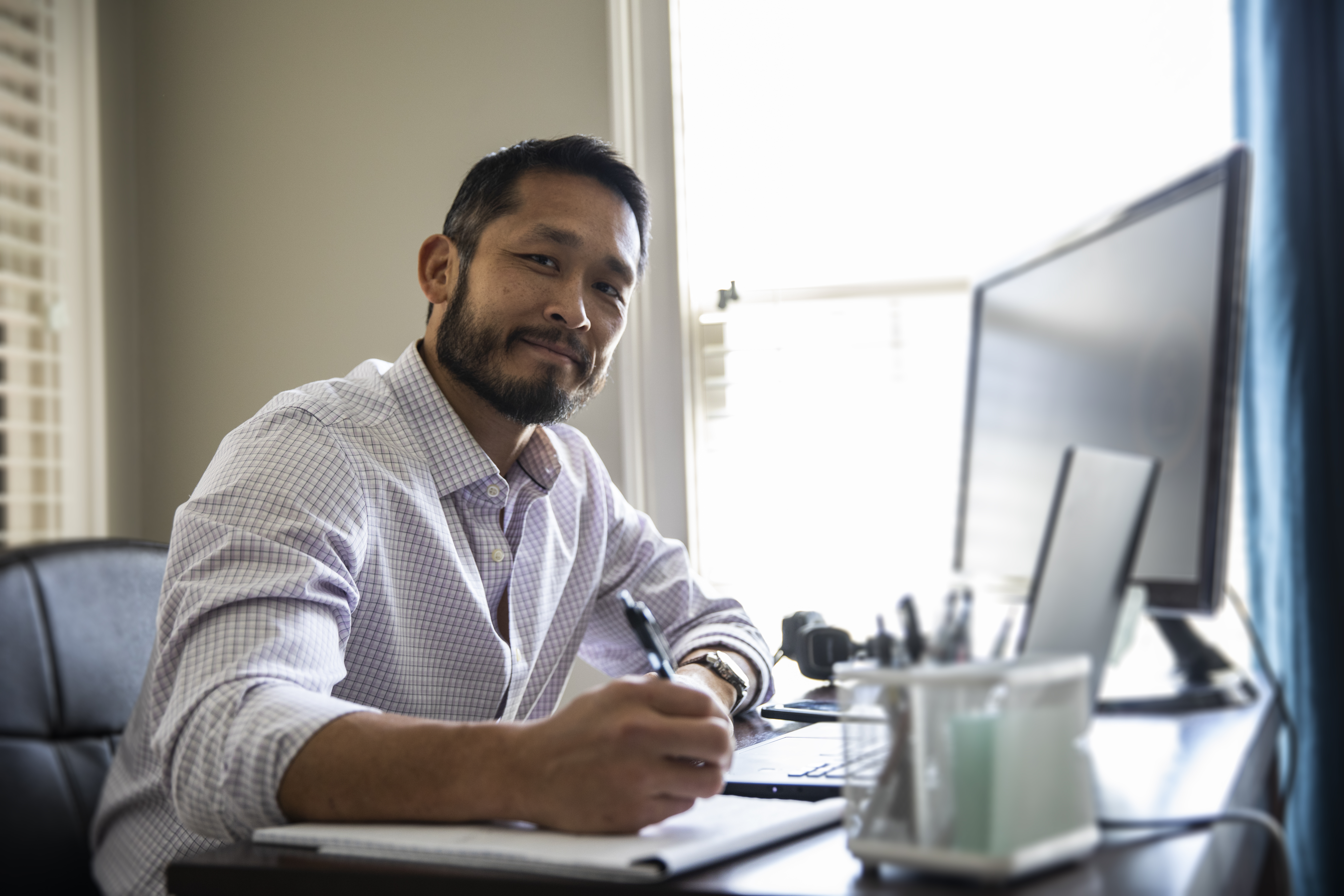 A man writing on a notepad while sitting at a computer desk