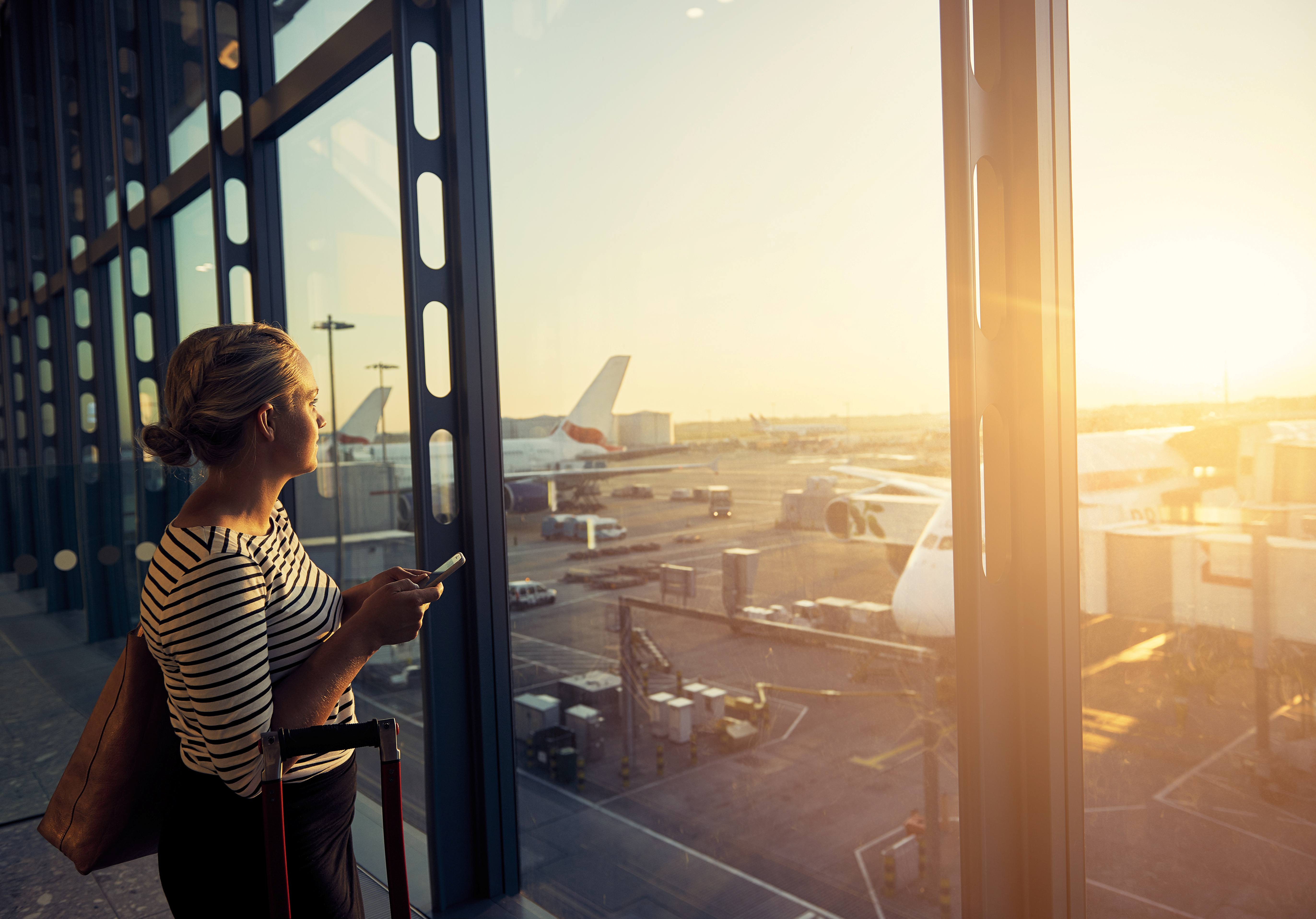 traveller with suitcase at airport, watching planes out the window