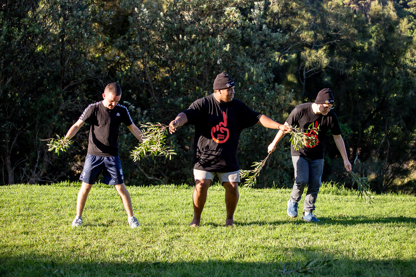Three young men outside on the grass performing an indigenous ceremony