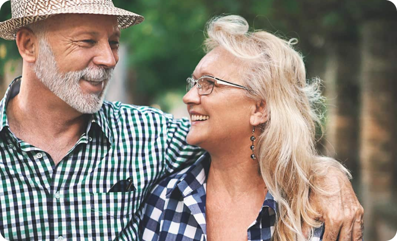Smiling senior couple embracing outdoors, man wearing straw hat and checked shirt, woman with glasses and blonde hair