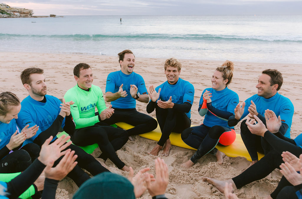 A group of surfers sitting in a circle at the beach clapping