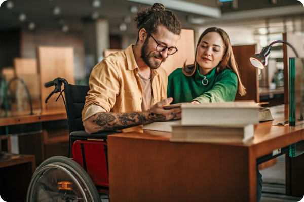 man in wheelchair and women sitting together reading a book