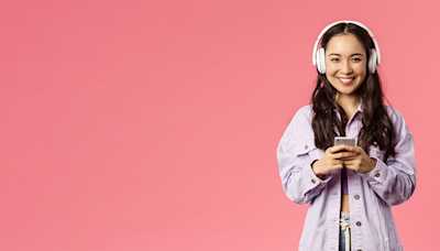 A woman smiling while wearing headphones and listening to a podcast