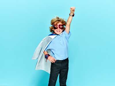 Primary school child dressed as super hero with arm raised in the air