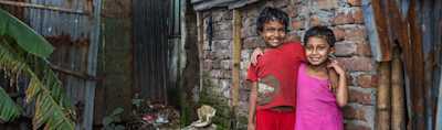two children pose next to a house