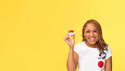 A woman smiling and holding up a red nose in the shape of a fox.