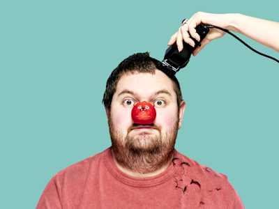 Person wearing red nose and getting their head shaved