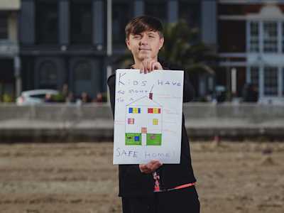 A boy holding up a sign that says "Kids have a right to a safe home."
