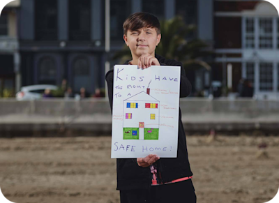A boy holding up a sign that says "Kids have a right to a safe home."