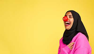 A woman laughing and wearing a red nose.