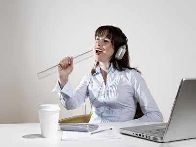 Woman sat at a desk singing into a ruler