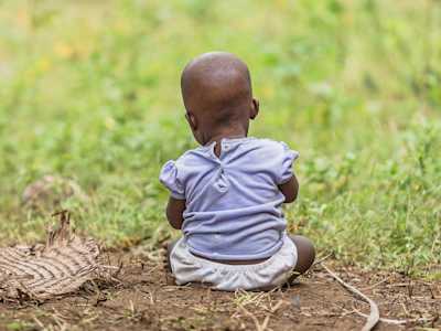 A toddler sat on the grass facing away from the camera